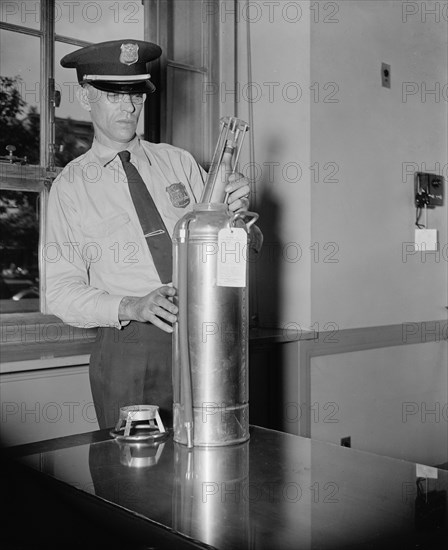 An officer in the Justice Department Guards, examines a new type of fire extinguisher cartridge, the cartridge is filled with carbon dioxide gas circa 1937.