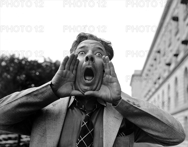 Close up of a man practing his hog calling, but looking like an angry man circa 1937.