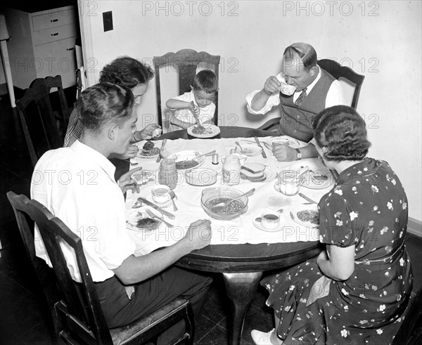 Family eating a meal together at the dinner table circa 1937.