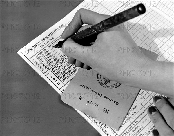 Entry being made in a budget book with bank book underneath hand circa 1940 .