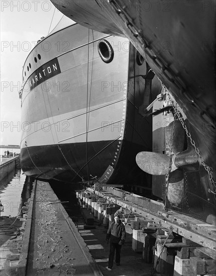 Dutch man stands between two ships in a shipyard or dock circa October 20, 1947.