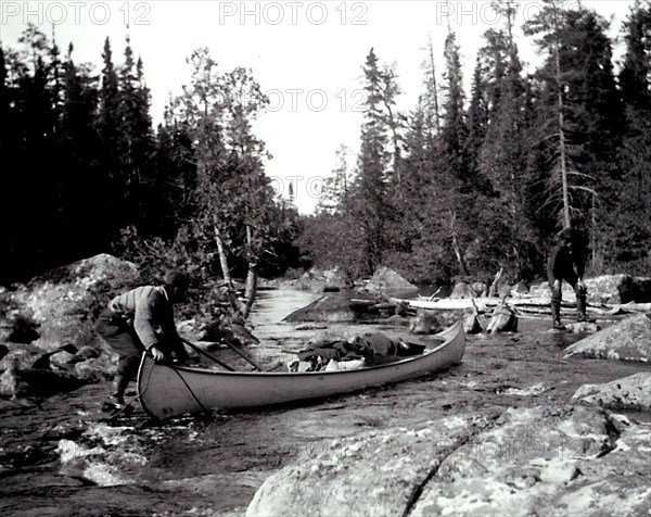 Two men manoeuvering a canoe down a set of rapids, possibly on the Lady Evelyn River, Ontario circa 1909.