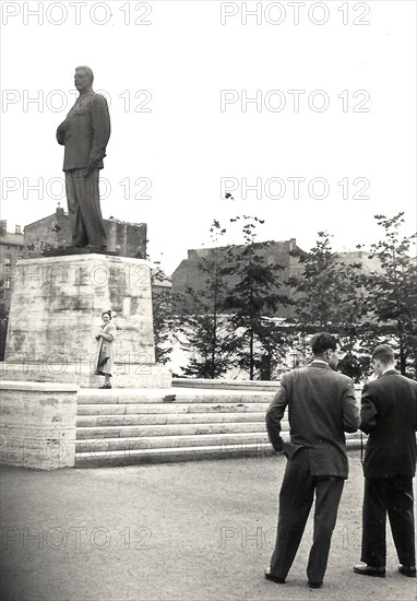 Photograph of two men and a woman in front of the former statue of Joseph Stalin on what is now Karl Marx Allee in Berlin, taken in 1955 (statue removed in 1961?) .