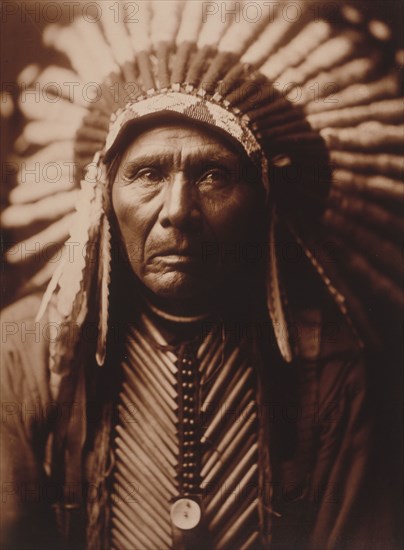 Edward S. Curtis Native American Indians - Three Horses, head-and-shoulders portrait, facing front, wearing headdress circa 1905.
