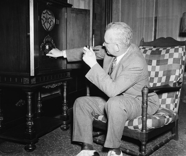 Man sitting in chair listening to a radio and tuning the radio circa 1936.