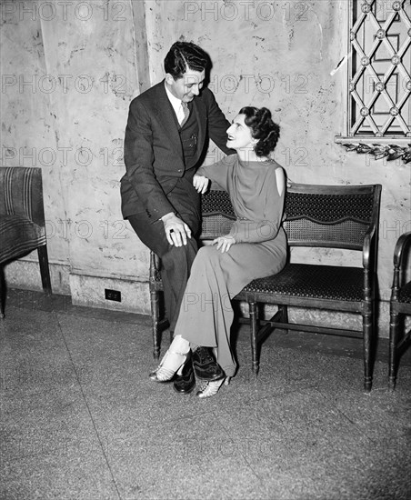 Man with woman who is sitting on a bench wearing a gown circa 1935.