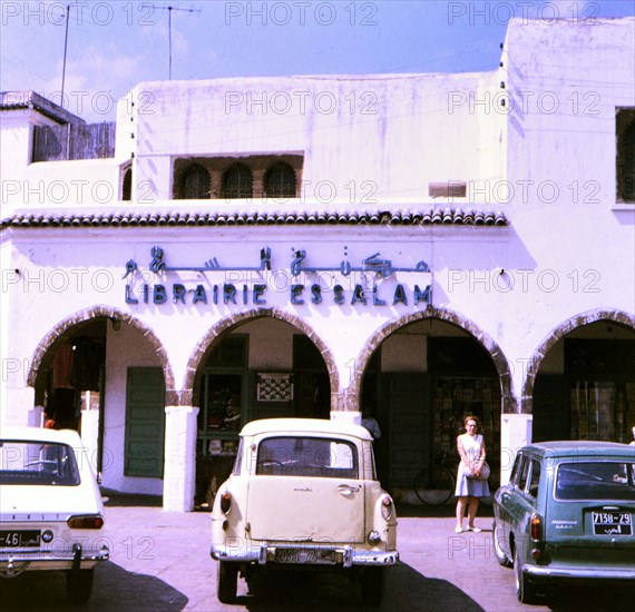 Woman standing outside a library near parked cars in Casablanca Morocco circa 1969.