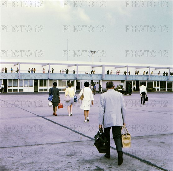 Passengers with luggage walking across the tarmac at an airport, probably the Casablanca Airport circa 1969.