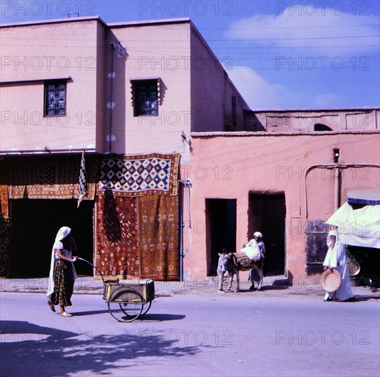 Woman pushing a two wheeled cart down the street in Marrakesh Morocco circa 1969.