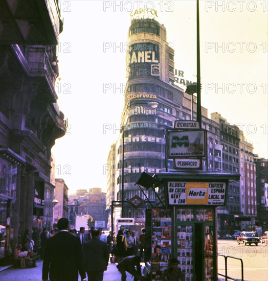 Pedestrians walking past a newstand in Madrid Spain circa 1969 .
