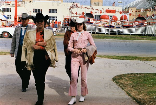 1960 Ft. Worth Stock Show - Well dressed visitors to the Fort Worth Stock Show - Tilt-a- Whirl amusement ride in the background.