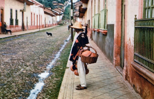 Mexican man in a small city in Mexico looking down a street at dogs circa 1950-1955 .