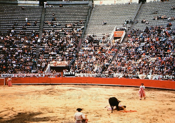 Half filled stadium of spectators watch a bull fight in Mexico circa 1950-1955.