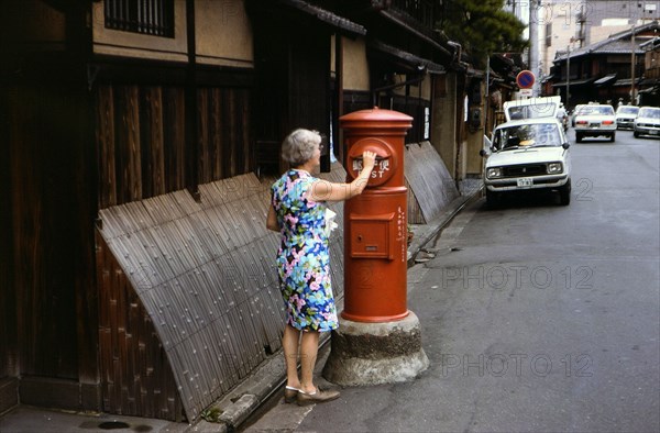 Woman mailing letters in a postal service mailbox in Kyoto Japan circa 1976.