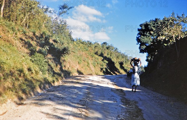 1962 Guatemala - Woman carrying food or package on her head down road to a village in Guatemala.