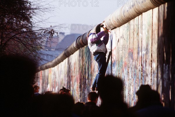 A West German man uses a hammer and chisel to chip off a piece of the Berlin Wall as a souvenir.  A portion of the Wall has already been demolished at Potsdamer Platz..