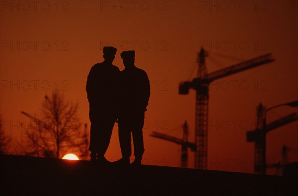 East German policemen stand atop a section of the Berlin Wall at sunset..