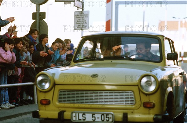 West German children applaud as an East German couple drive through Checkpoint Charlie and take advantage of relaxed travel restrictions to visit West Germany..