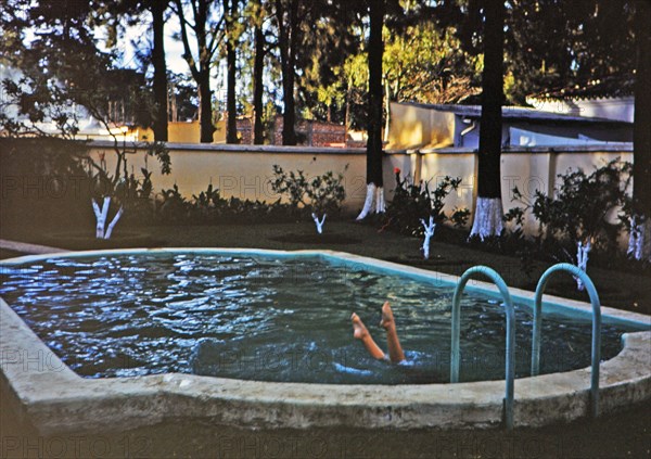 Swimmer in pool, legs sticking out of water circa 1960-1963.