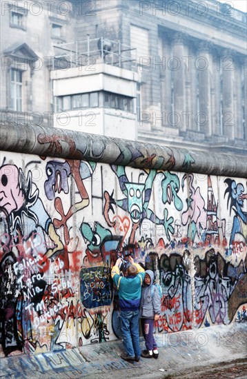 West German children attempt to chip off a piece of the Berlin Wall as a souvenir. A portion of the Wall has already been demolished at Potsdamer Platz..