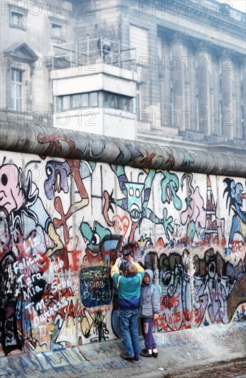 West German children attempt to chip off a piece of the Berlin Wall as a souvenir.  A portion of the Wall has already been demolished at Potsdamer Platz..