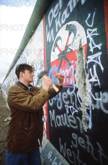 A West German man uses a hammer and chisel to chip off a piece of the Berlin Wall as a souvenir.  A portion of the Wall has already been demolished at Potsdamer Platz..