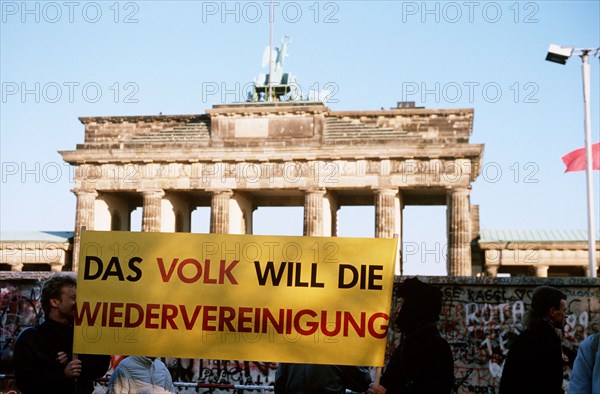 West German citizens display a banner as they maintain a vigil for the demolition of the Berlin Wall at the Brandenburg Gate.  A portion of the Wall has already been demolished at Potsdamer Platz..