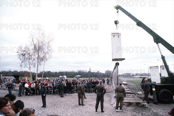 East German police and West German citizens watch as a workman dismantles a section of the Berlin Wall at Potsdamer Platz..