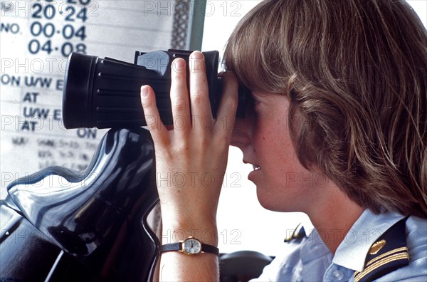 1980s Coast Guard - A female lieutenent junior grade officer piers through a pair of binoculars while on operations duty.