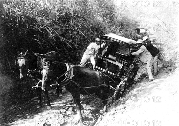 Horse drawn cart stuck in mud and people helping to dislodge it