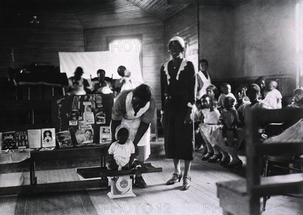 Preschool child is weighed by African American nurse