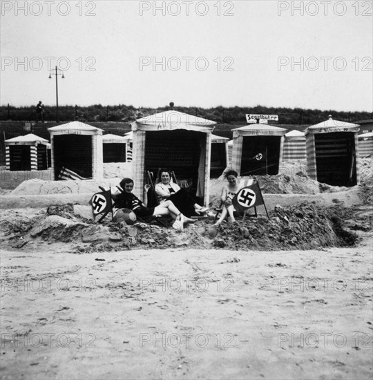 Women at beach in Germany with Nazi swastika flags planted in the sand