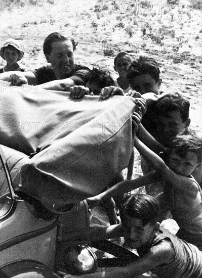 Boys help man push car stuck in sand of a beach near Viareggio