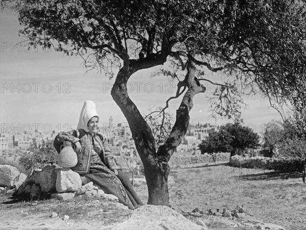 Bethlehem woman with jar seated under almond tree. Bethlehem in background ca. between 1934 and 1939
