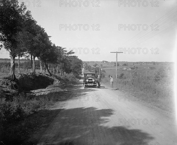 Two men standing outside a car on a rural road ca.  between 1910 and 1926