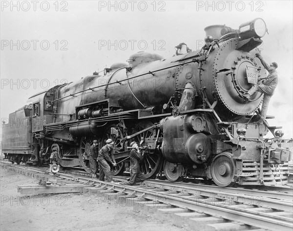 Workers conducting maintenance on a train locomotive ca. between 1909 and 1940