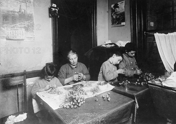 A woman and her children making artificial flowers in a New York tenement house ca. between 1909 and 1919