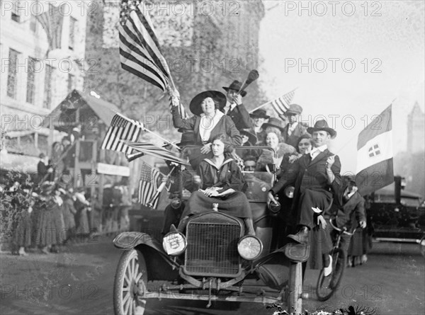Men and women in an overcrowded car waving American flags during a peace demonstration ca.  1918