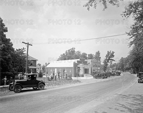 Early 1900s street scene, car driving down a road in small town ca. between 1918 and 1928