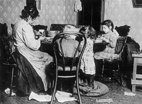 Children, ages 4, 6 and 9, picking nuts in a basement tenement; filth abounds and room is dark & damp. ca. between 1909 and 1919