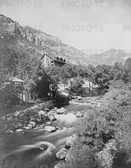 A rushing creek in foreground and buildings in the background at Estes National Park, Colorado ca. 1909