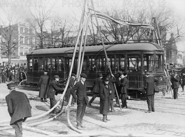 Firemen with hoses stretched over a streetcar ca. 1909