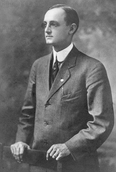 Photographer Herbert E. French, half-length portrait, standing, facing left, hands on back of chair ca. 1909