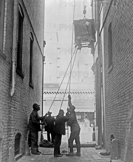 Three African American men lifting a piece of equipment, with block and tackle, at the Standard Engraving Company ca. 1909