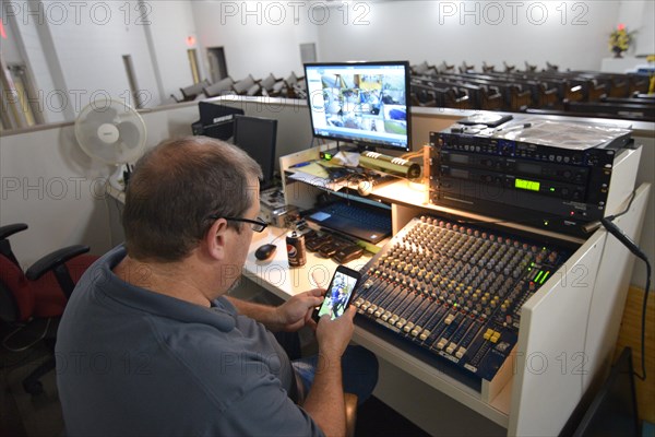 During the Covid-19 pandemic, some churches chose to record sermons to play on their websites and through streaming services to replace in person worship. Here, a deacon in the sound booth looks at his cell phone as a minister has his Sunday morning sermo