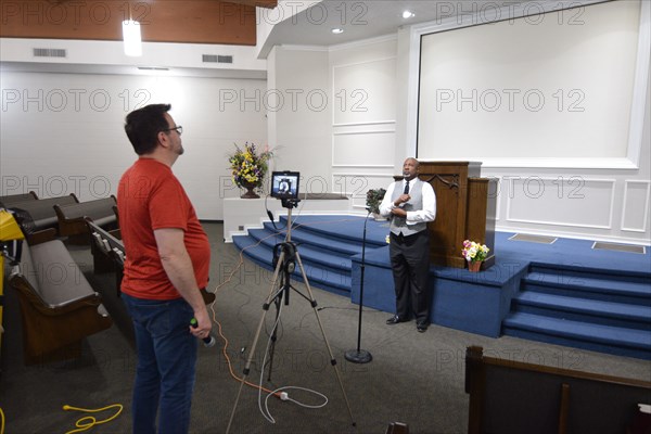 During the Covid-19 pandemic, some churches chose to record sermons to play on their websites and through streaming services to replace in person worship. Here, a technician records a minister as he preaches to the camera.