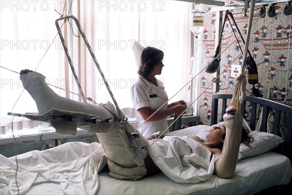 A nurse adjusts the intravenous feeding line on a patient lying in traction