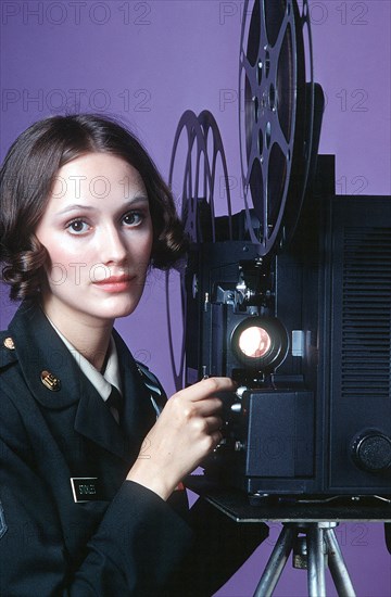 A female U.S. Army audiovisual technician operates a 16mm film projector.