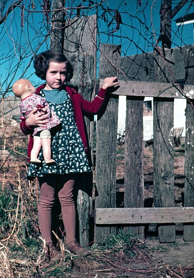 Girl with doll standing by fence