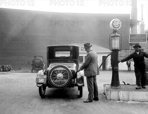 Man pumping gas into his automobile in early 1900s